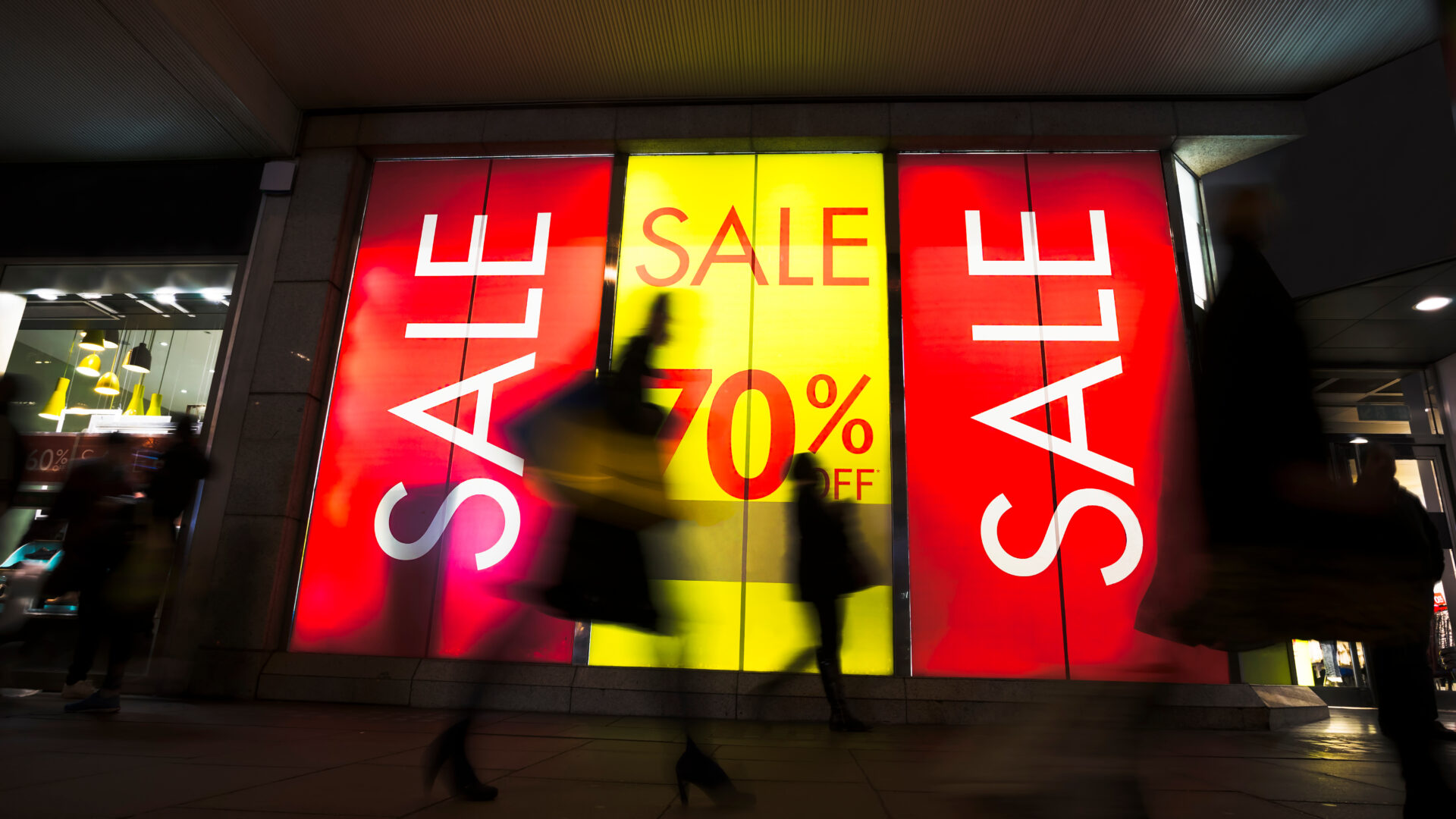 Sale signs in shop window, include silhouette of shoppers